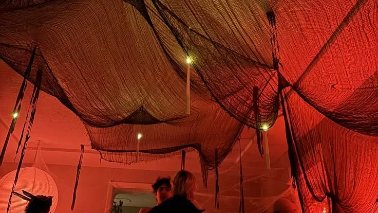Black gauze and candles hanging from a ceiling over guests in costume, lit red