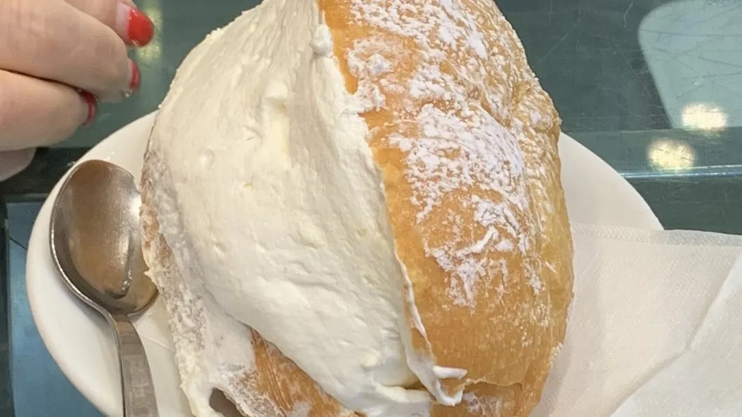 A maritozzo overflowing with whipped cream on a plate at a Roman coffee bar