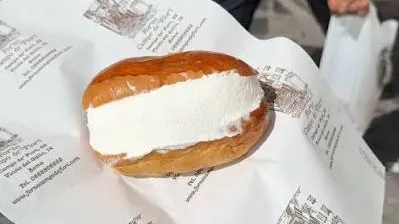 A maritozzo filled with cream, held on Forno Campo de' Fiori's printed paper