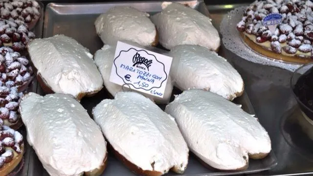 A tray of maritozzi con panna behind the glass at Pasticceria Regoli, with the shop's price card