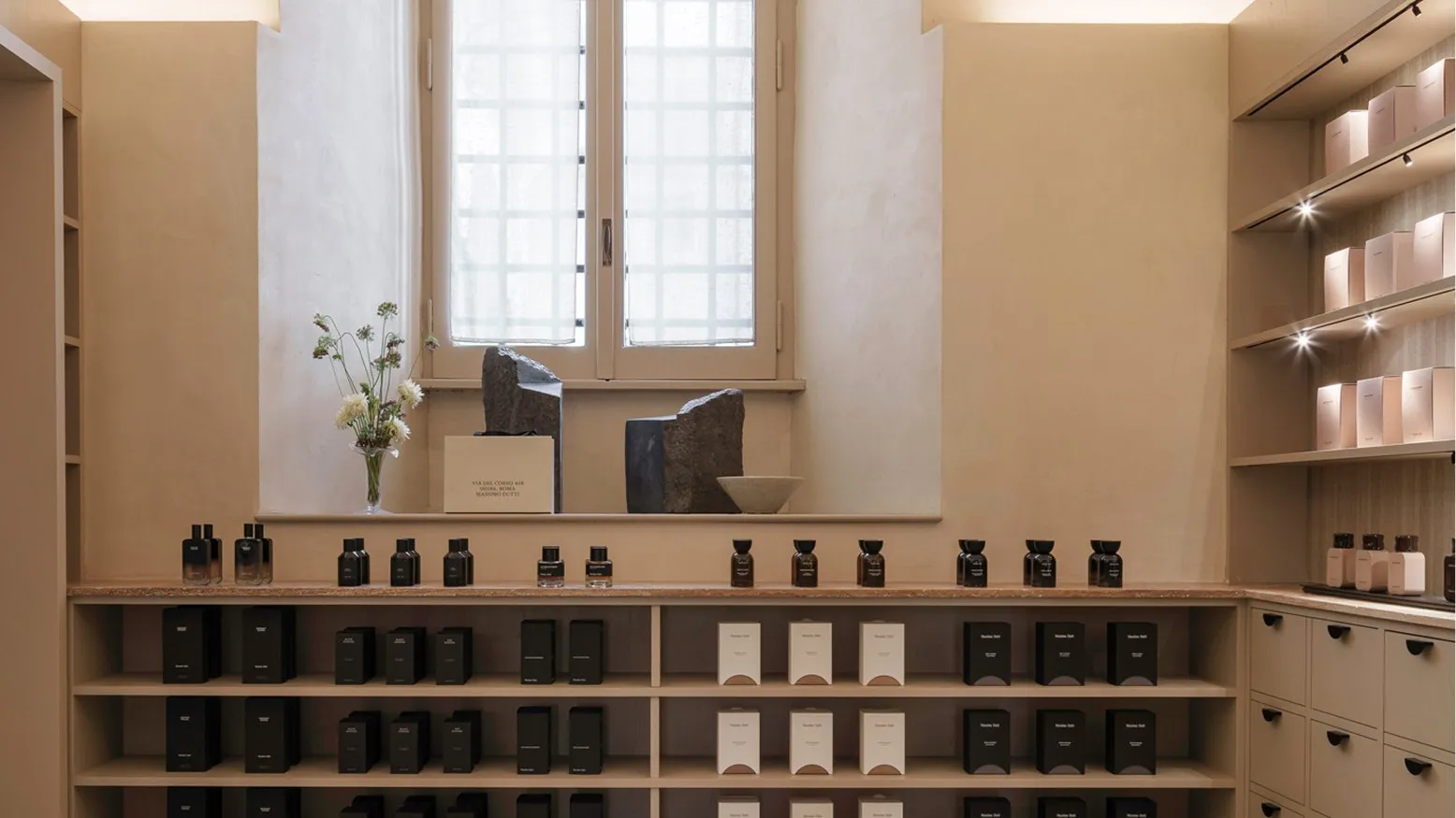 A vaulted room of fragrance bottles and boxes on wooden shelves beneath a tall window