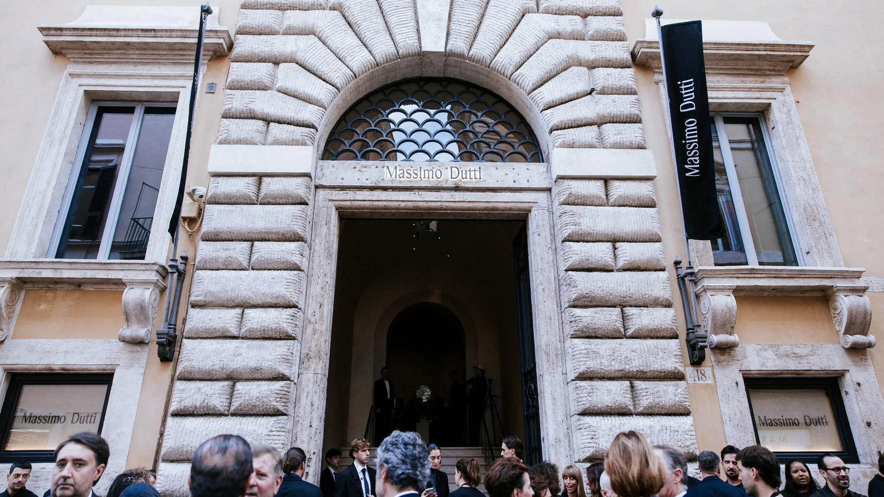 Guests gathered on the pavement outside the rusticated stone portal of Palazzo Ruspoli, with black Massimo Dutti banners either side of the door