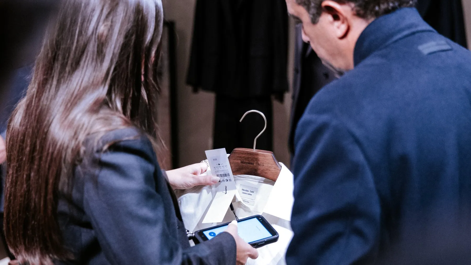 Two guests examining a white shirt on a wooden Massimo Dutti hanger, its Limited Edition label visible