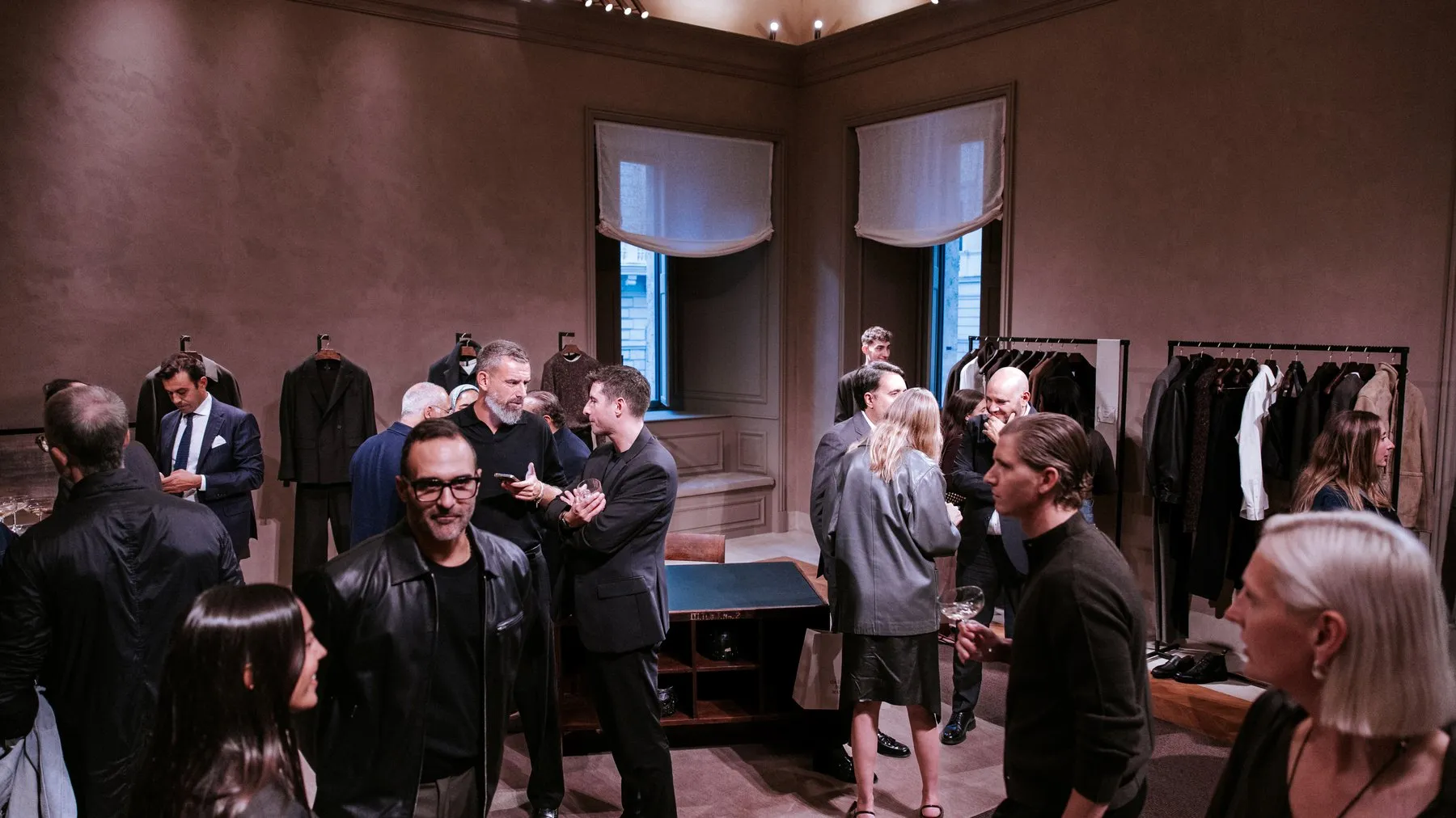 Guests talking in a high-ceilinged room with clothing rails and tall windows