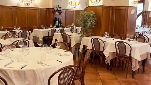 A wood-panelled dining room at Dal Toscano, with round tables laid in white and a terracotta floor