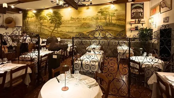 A dining room at Taverna Trilussa with a painted landscape mural and wrought-iron screens between the tables